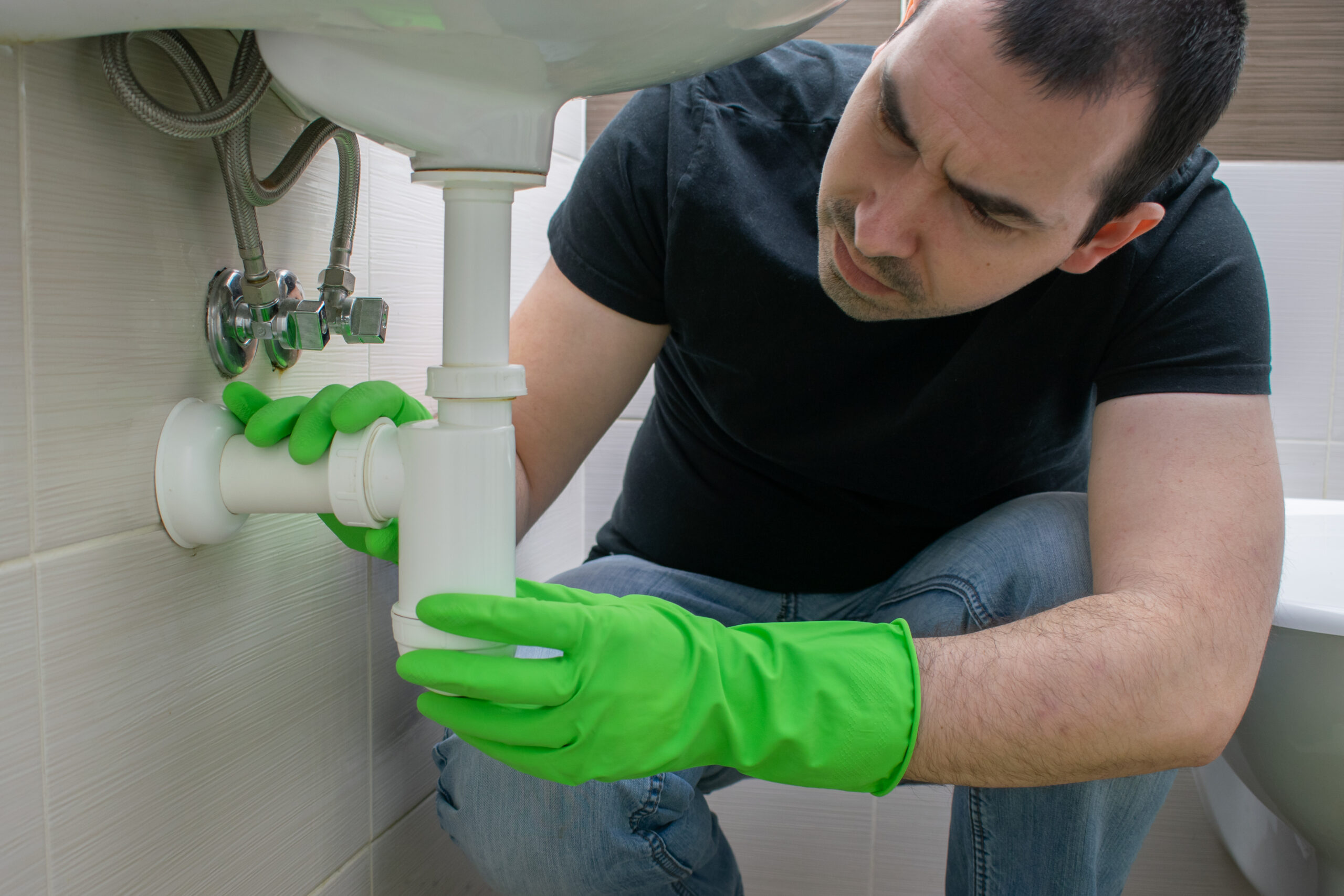 Homeowner inspecting under-sink pipes in Regina.