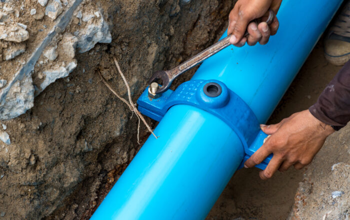 A plumber tightening a fitting on a new blue sewer pipe during an underground replacement or repair.