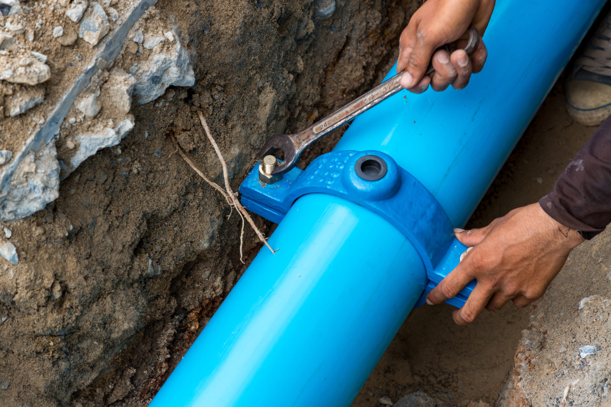 A plumber tightening a fitting on a new blue sewer pipe during an underground replacement or repair.